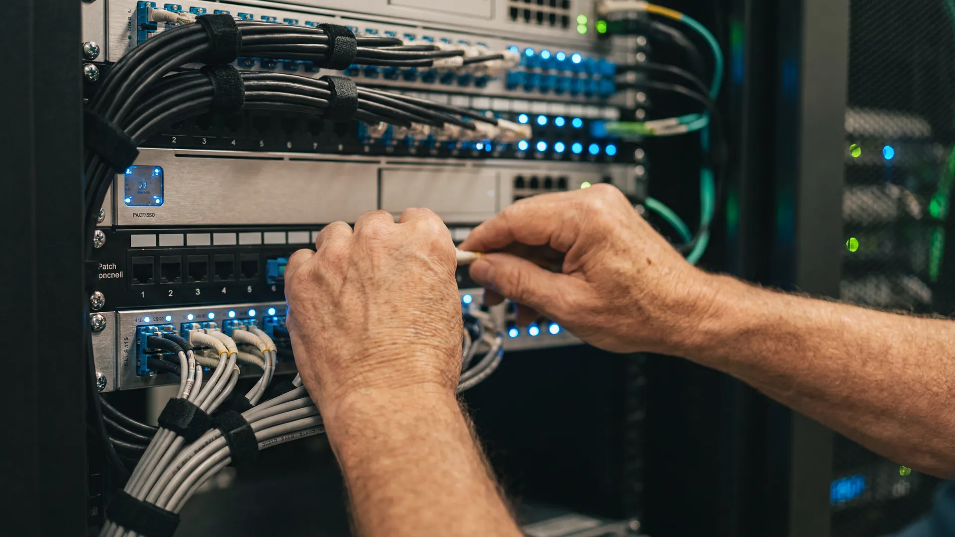 Manos expertas de un ingeniero conectando fibra &oacute;ptica en un panel de telecomunicaciones